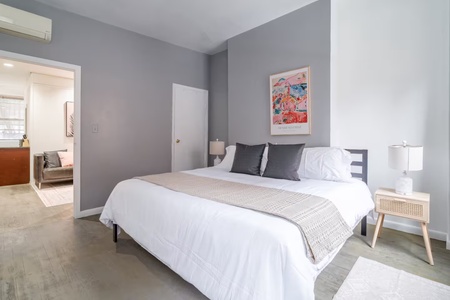 Sink into crisp white linens and soft pillows in your serene bedroom retreat, where gray walls and modern art create the perfect backdrop for restful nights.