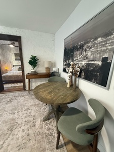 Your intimate dining nook invites quiet meals beneath striking cityscape art, where warm wood meets sage velvet in perfect harmony.