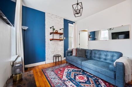 Unwind in your stylish living space with bold blue accents, exposed brick, and cozy seating perfect for evening relaxation.