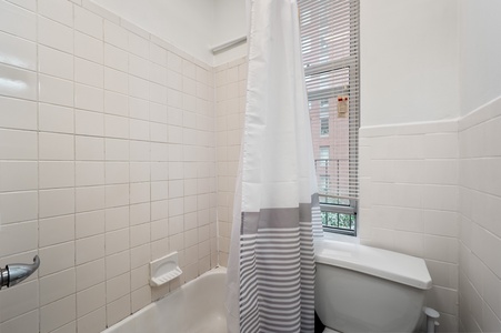 Step into your private spa-like bathroom where crisp white tiles and a deep soaking tub create the perfect retreat after exploring the city.