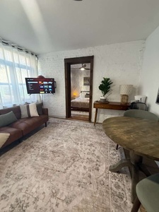 Settle into your cozy living space with exposed brick walls, modern furnishings, and natural light streaming through large windows.