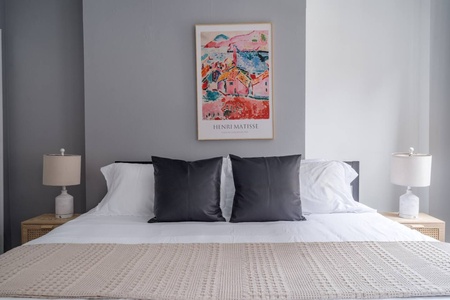 Slip into crisp white linens in your stylish bedroom, where modern design meets comfort beneath beautiful artwork.