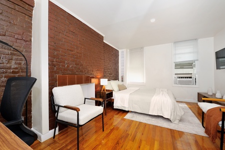 Relax in your stylish bedroom featuring exposed brick walls, polished hardwood floors, and crisp white linens for ultimate comfort.