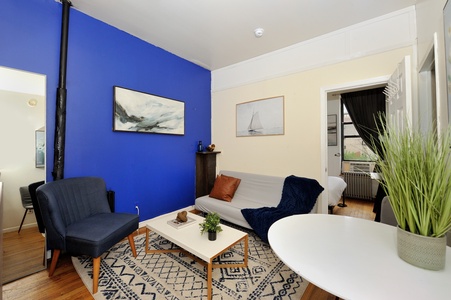 Sink into your comfortable sofa in this stylish living room featuring vibrant blue walls, cozy seating, and beautiful natural light streaming through.