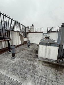 Rooftop terrace with iron railings overlooking neighboring buildings and urban rooftops in the surrounding area.