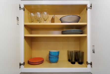 Your fully stocked kitchen cabinet awaits with colorful dishes, wine glasses, and dining essentials for memorable meals during your stay.