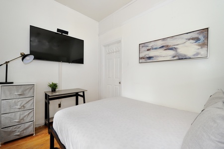 Unwind in your serene bedroom featuring crisp linens, modern artwork, and a wall-mounted TV for your evening entertainment.