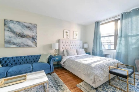 Relax in your stylish bedroom featuring a plush tufted bed, elegant blue sofa, and soothing coastal artwork that creates the perfect retreat.