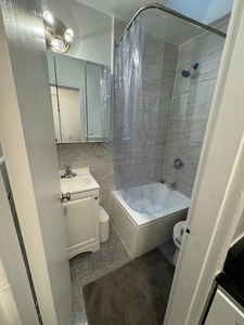 Step into your pristine bathroom featuring modern gray tiling, a spacious tub-shower combo, and clean white vanity - perfect for refreshing after your daily adventures.