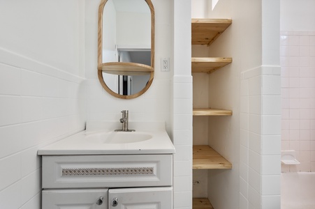 Your modern bathroom features a stylish oval mirror and built-in wooden shelving for all your essentials.