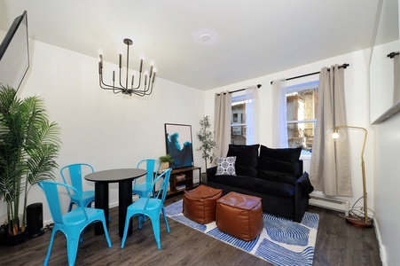 Relax in your stylish living space with vibrant turquoise dining chairs, plush navy sofa, and modern chandelier creating the perfect atmosphere.