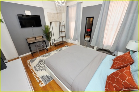 Unwind in your stylish bedroom featuring a wall-mounted TV, cozy seating area, and warm hardwood floors for ultimate relaxation.