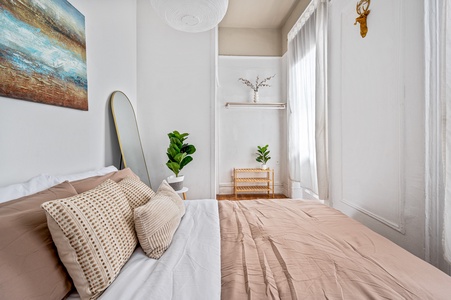 Drift off in your serene bedroom sanctuary with warm neutral tones, fresh greenery, and natural light streaming through elegant curtains.