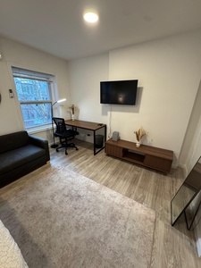 Unwind in your modern living space featuring a wall-mounted TV, stylish wood entertainment console, and dedicated workspace with ergonomic chair.