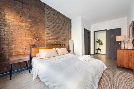 Rest peacefully in your stylish bedroom featuring exposed brick walls, crisp linens, and warm modern furnishings.
