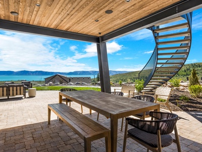 A covered patio with stunning mountain and lake views features rustic wood furnishings under a warm timber ceiling, creating an inviting outdoor dining and relaxation space.