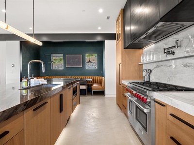 Sleek modern kitchen with professional-grade stove, marble backsplash, and warm wood cabinetry—perfect for preparing gourmet meals. Stylish dining nook beyond invites relaxed gatherings.
