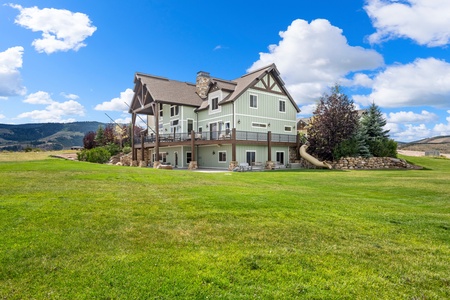 A mountain lodge-style property sits surrounded by expansive lawns and open fields, with forested hills providing a scenic backdrop to the natural setting.
