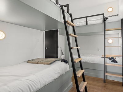 Your modern bunk room features sleek steel frames with cozy white linens and warm wood accents, perfect for families or groups seeking stylish comfort and space efficiency.