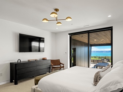 Sink into your plush bed while gazing at stunning ocean views through the floor-to-ceiling glass doors. A sleek modern retreat with coastal elegance awaits.