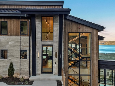 Contemporary architectural design blends wood and stone with dramatic floor-to-ceiling windows, showcasing proximity to mountain and water landscapes.