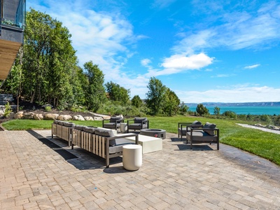 Stunning waterfront property featuring expansive outdoor entertaining areas with breathtaking lake views, manicured lawns, and native trees under brilliant blue skies.
