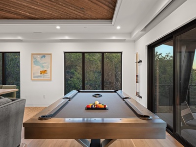 You'll love unwinding here—a sleek billiard table under warm wood-beamed ceilings, natural light spilling through floor-to-ceiling windows, and a seamless flow to your outdoor space.