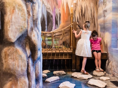 This vibrant play area features an enchanting cave-themed bridge where young adventurers can explore stepping stones and rope railings, perfect for imaginative family fun.