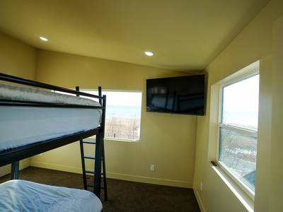 Your cozy bedroom features a space-saving bunk bed and flat-screen TV, with large windows framing peaceful countryside views.