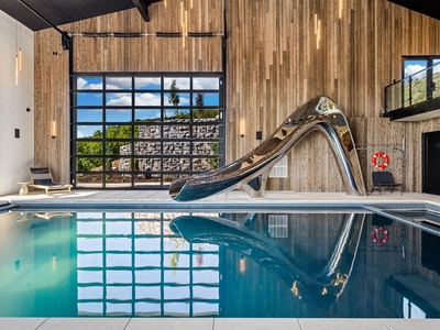 Picture yourself diving in from the gleaming slide, splashing into your private indoor pool beneath soaring ceilings and sunlit windows. Warm wood walls and modern design create a luxurious, playful escape just for you.