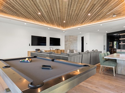 A stunning entertainment space featuring a striking wood-slat ceiling with ambient lighting, where you can challenge friends to billiards or gather on plush seating beneath twin TVs—a perfect blend of style and fun.