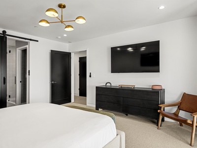 Unwind in your serene bedroom featuring a plush bed, warm brass chandelier, and modern comforts including a flat-screen TV and sleek furnishings designed for your ultimate relaxation.