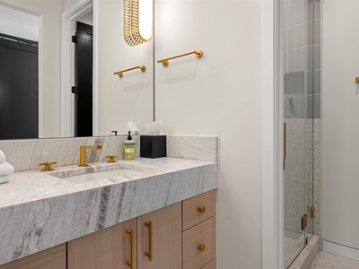 Step into your private bathroom featuring elegant marble countertops, warm gold fixtures, and a spacious glass-enclosed shower—perfect for unwinding after a day of exploring.