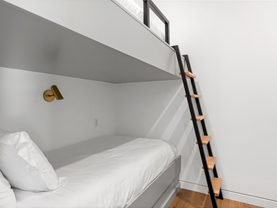 Your cozy sleeping nook features crisp linens, modern brass sconces, and a sleek ladder to the loft above—perfect for restful nights in this thoughtfully designed space.