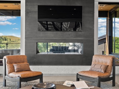 Settle into your modern living space with cozy leather chairs and a striking fireplace, framed by scenic views that bring nature right into your retreat.