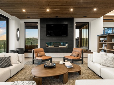 Sink into plush sofas facing a sleek fireplace and widescreen TV, surrounded by floor-to-ceiling windows framing scenic mountain views—your perfect retreat after exploring.