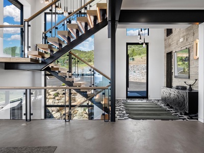 Step into soaring architectural beauty with striking open stairs and walls of windows revealing tranquil hills and pool views beyond your modern sanctuary.
