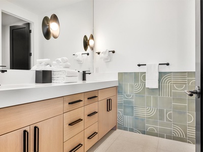 Step into your sleek, modern bathroom featuring custom geometric tiles and warm wood vanity. Plush towels await, while artistic lighting adds a stylish touch to your daily routine.