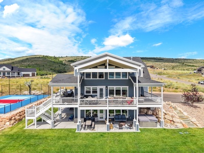 Modern mountain home with multiple outdoor decks, sports court, and hot tub nestled in scenic rolling hills.