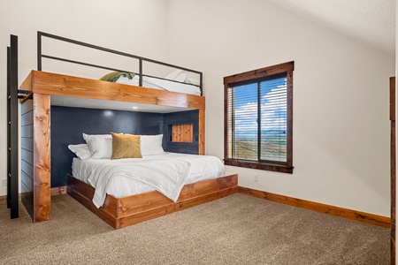 Your bedroom offers a striking bunk bed with a custom wood and metal frame, plus crisp linens and a window that frames sweeping views of open terrain beyond.