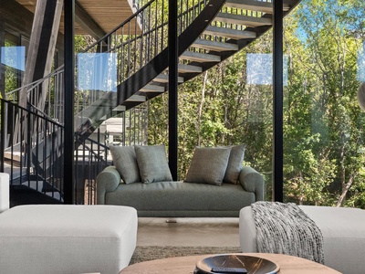 Unwind in your sleek living space, where floor-to-ceiling windows frame serene forest views. Sink into plush seating beneath a dramatic floating staircase, connecting you to nature's tranquility.