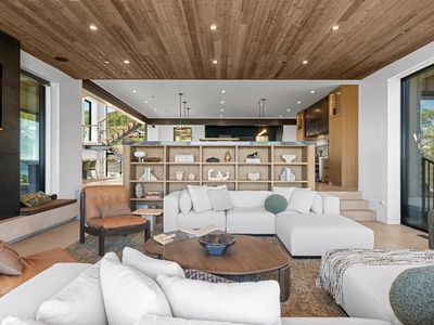 Sink into plush seating beneath stunning wood ceilings as natural light pours through expansive windows, creating your perfect gathering space with open views to the chef's kitchen.