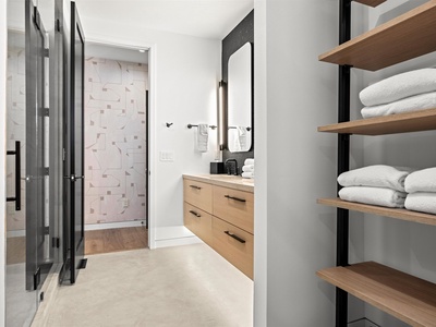 Your modern ensuite awaits with sleek wood vanity, rainfall shower, and plush towels neatly arranged on open shelving for a spa-like escape.