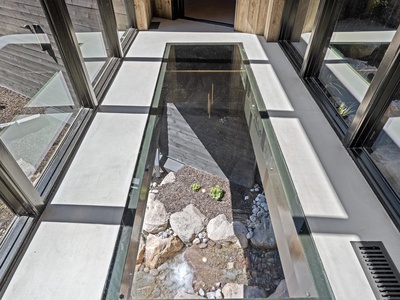 A unique architectural feature showcases a glass floor panel revealing the natural landscape below, blending modern design with the surrounding terrain through floor-to-ceiling windows.