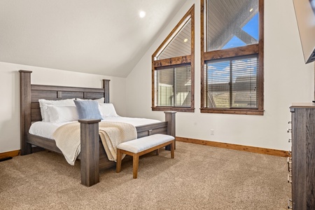 Rest easy in this serene bedroom, where vaulted ceilings and sunlit windows frame peaceful views. Wake to soft morning light and cozy textures that wrap you in comfort.