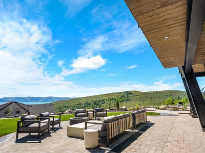A spacious covered patio features contemporary lounge seating overlooking scenic rolling hills and a distant lake, ideal for outdoor relaxation and entertaining.