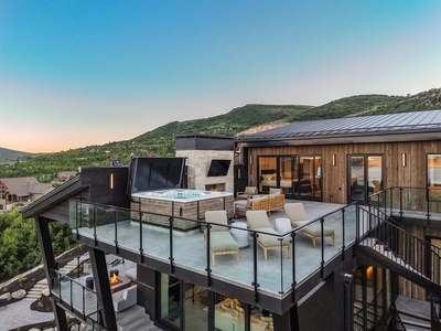 A stunning hillside property with modern architecture set against a dramatic natural landscape, featuring a rooftop deck with hot tub and outdoor fireplace—ideal for sunset gatherings and mountain views.