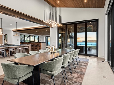 Gather around the elegant dining table beneath a stunning chandelier, where warm wood tones meet modern design. Floor-to-ceiling windows frame breathtaking water vistas, connecting your indoor dining to the serene outdoor beauty.