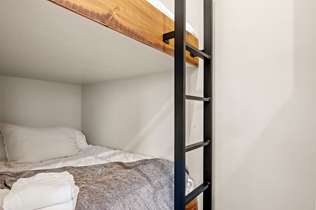 Your cozy bunk setup features modern metal ladder access, warm wood accents, and soft linens—perfect for restful nights and extra sleeping space.