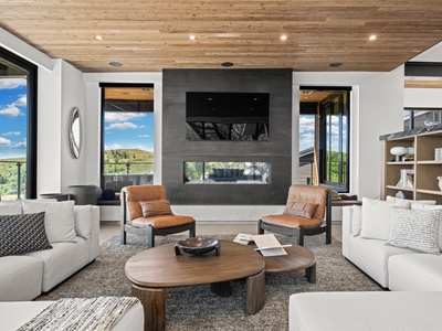 Sink into plush seating before a double-sided fireplace framed by sweeping mountain views. Warm wood ceilings and modern design create your perfect retreat.